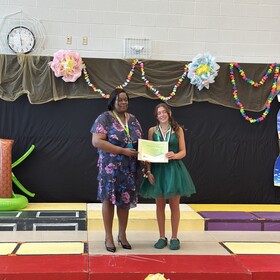 Fête des finissants de 8e année, la direction d'école prend la pose avec une élève qui tient son certificat